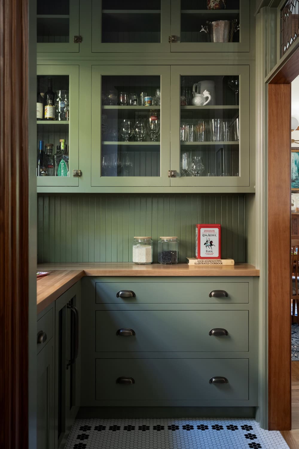 Green pantry with efficient storage, glass front cabinets, and hexagonal flooring honoring the 1902 home.